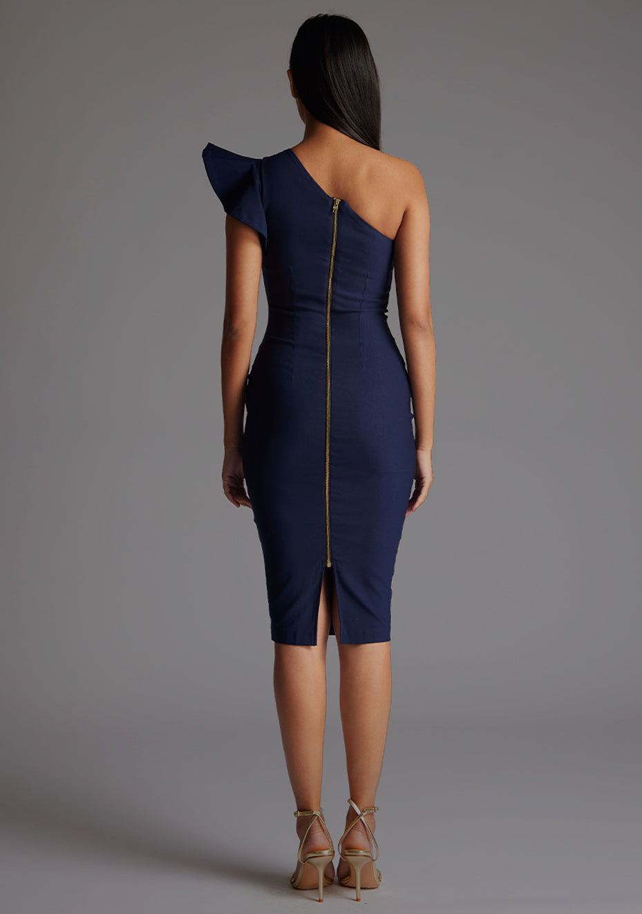 Back image of a model wearing a navy one shoulder midi dress with a stunning one-shoulder design with ruffle detail and an asymmetric neckline, all tied together with a gold centre back zip. The design featured is the Vesper Zanab Navy One Shoulder Midi Dress.