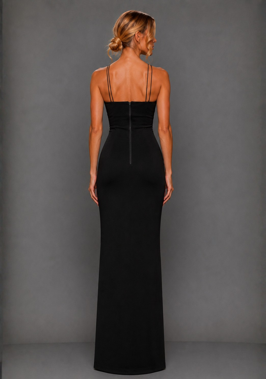 Back image of a model wearing the VSPR Auralia High Neck Strappy Black Maxi Dress, showcasing the sleek fitted silhouette and minimalist back zip against a grey studio backdrop.