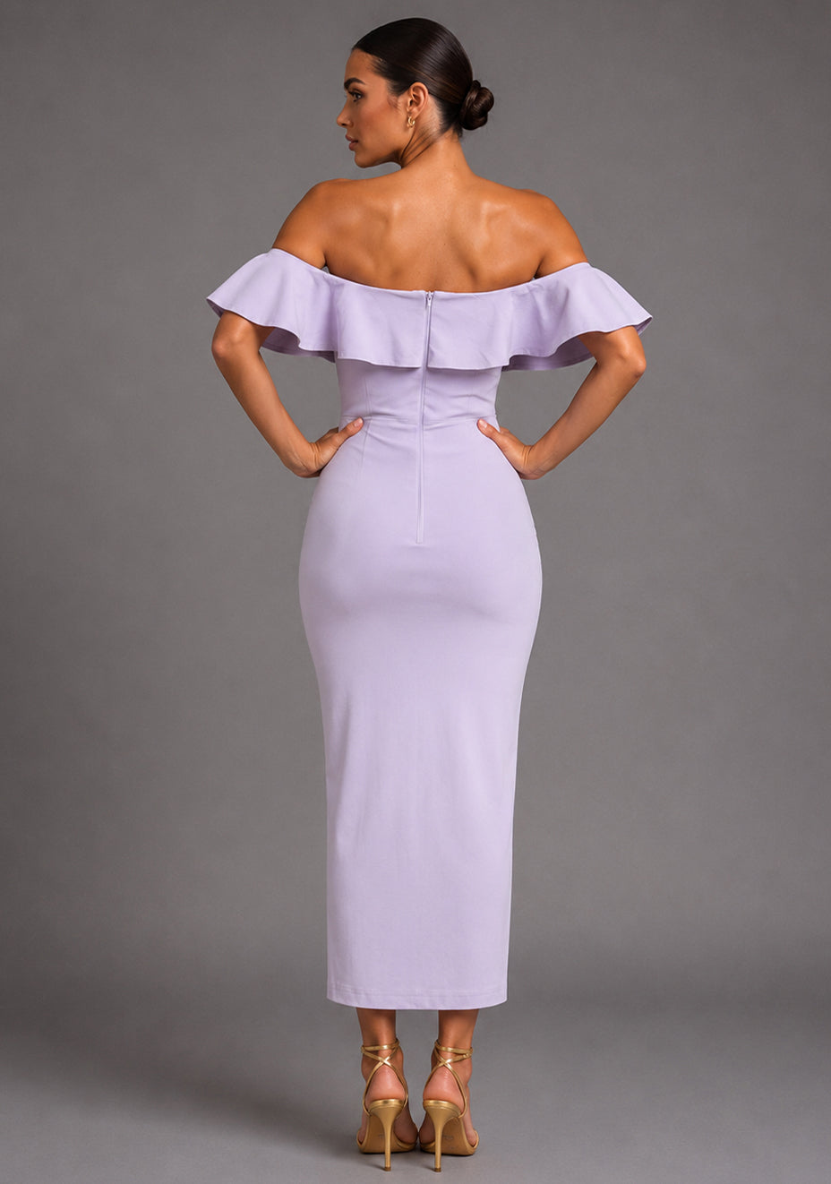Back image of a model wearing the VSPR Deirdre Bardot Off-Shoulder Frill Lilac Midaxi Dress showcasing the off-shoulder Bardot neckline, feminine frill detailing, and sleek fitted silhouette against a grey studio backdrop.