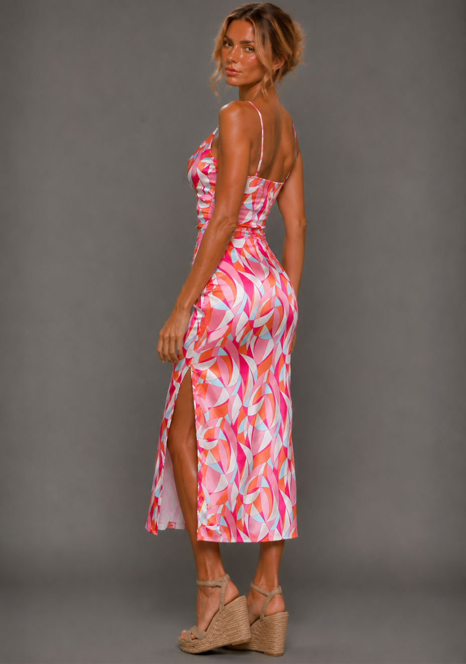 Side back image of a model wearing the VSPR Harper Geo Print Satin Midaxi Dress showcasing the figure-skimming silhouette, elegant midaxi length, flowing side split, and colourful geometric satin pattern against a grey studio backdrop.