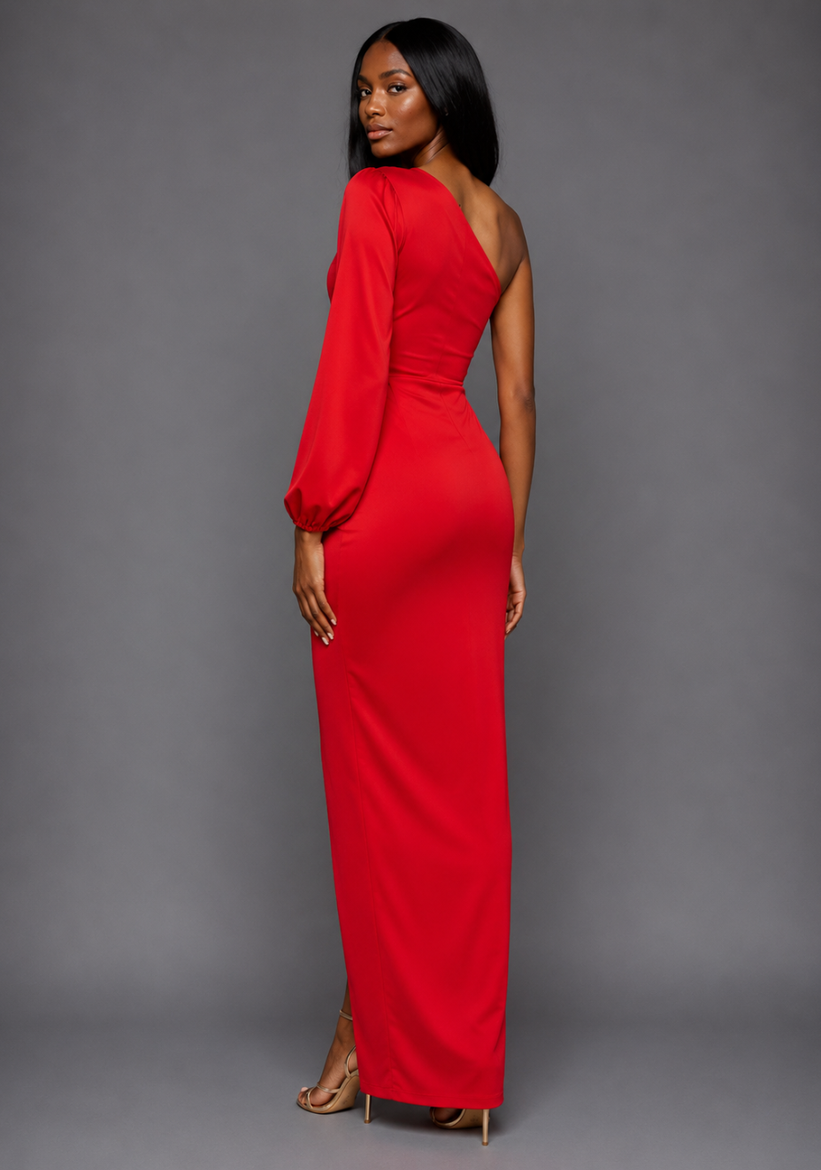 Side-back image of a model wearing the VSPR Keaton One Sleeve Red Maxi Dress, highlighting the sleek silhouette and flowing maxi length from a side angle against a grey studio backdrop.