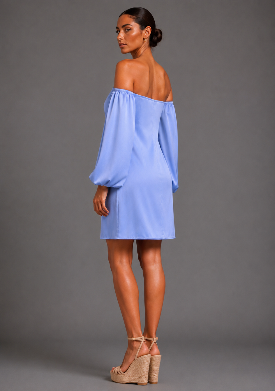 Back angled view of a model wearing the Vesper Kirby Bardot Long Sleeve Blue Mini Dress displaying the off-shoulder neckline and blouson sleeves.
