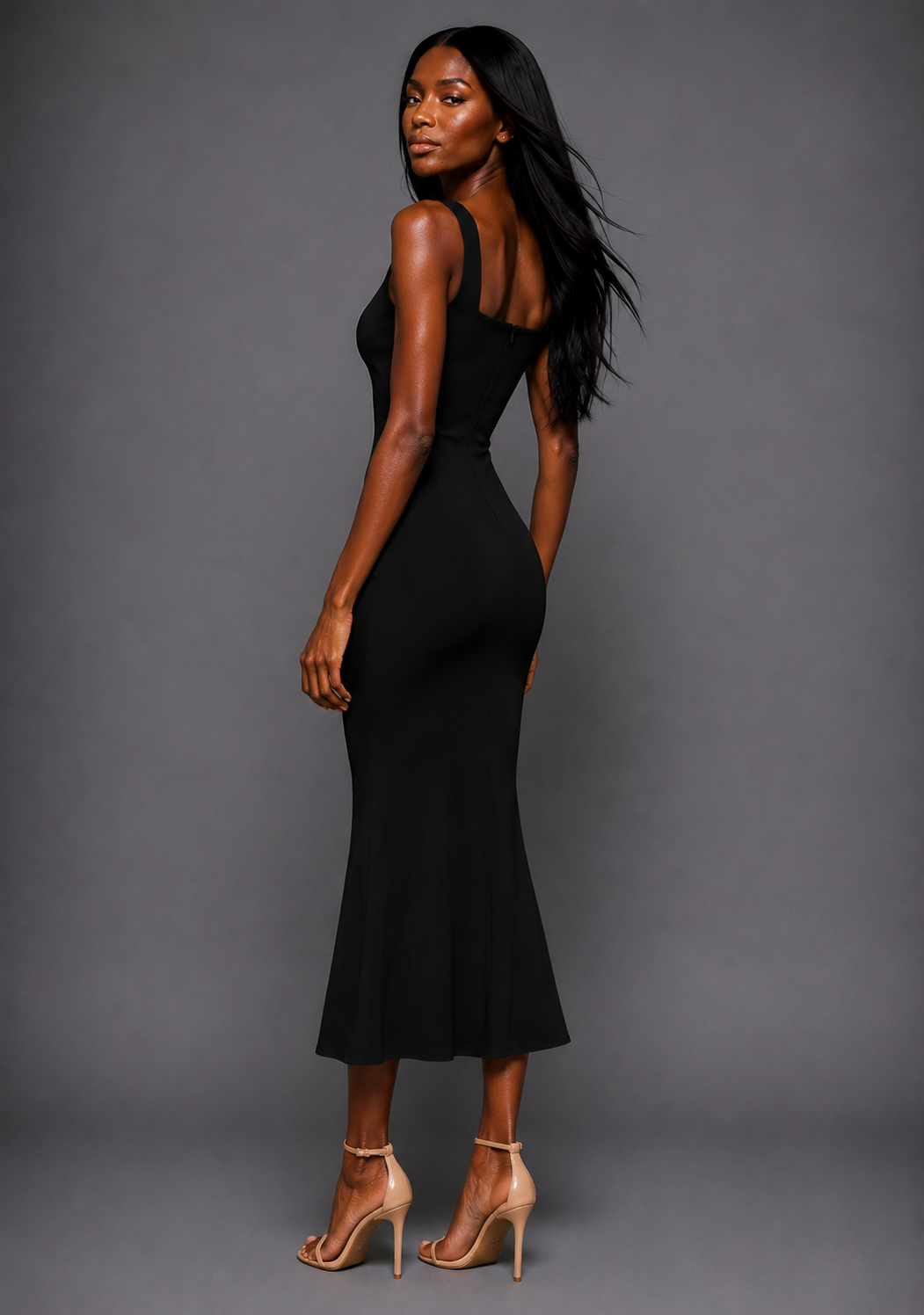 Side back image of a model wearing the VSPR Marianna Square Neckline Fishtail Black Midaxi Dress showcasing the sculpted silhouette, wide shoulder straps, and graceful flared hem against a grey studio backdrop.