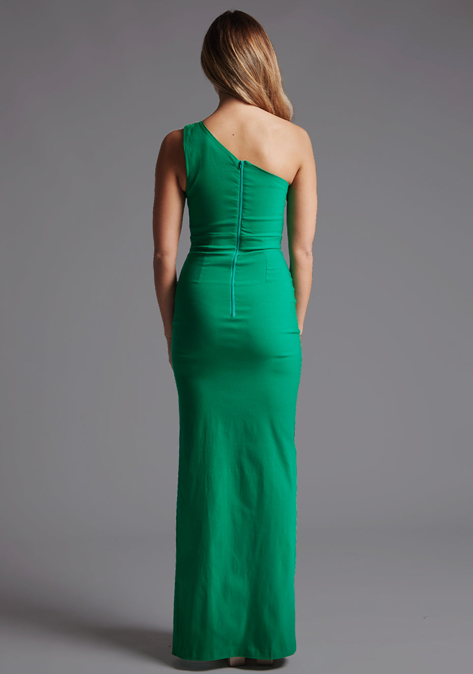 Back image of a model wearing a green one shoulder maxi dress with a   one-shoulder design, cut-out detail and centre back zip fastening.  The design featured is the Vesper Maya Emerald Green One Shoulder Maxi Dress.
