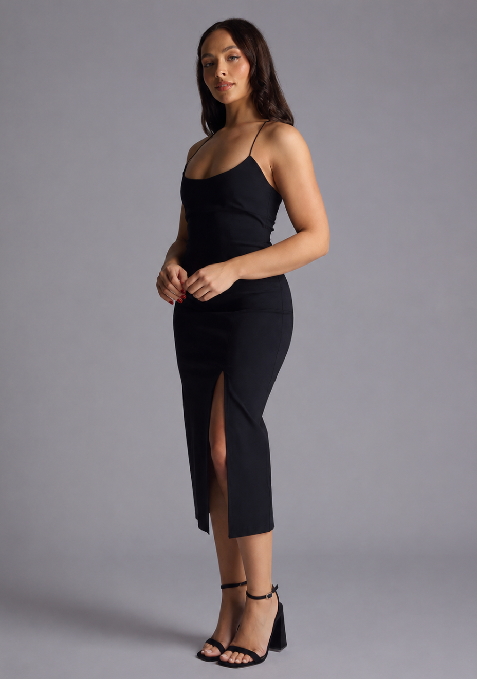 Woman wearing the Vesper Petite beryl black midaxi dress with a thigh slit on a grey background, side front view