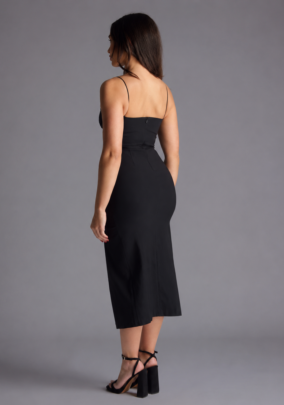 Woman wearing the Vesper Petite Tate black cami strap midaxi dress against a grey background, side back view