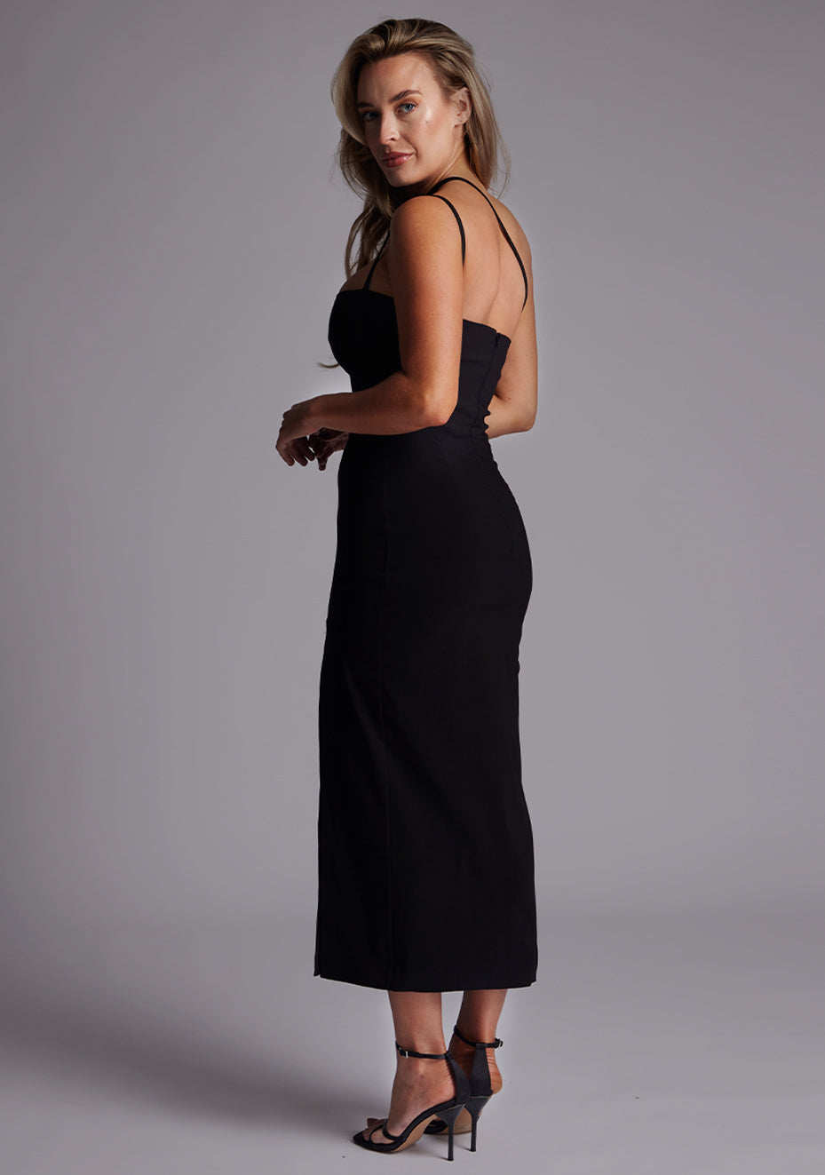 Side back image of a model wearing the Vesper Abigail Cross Strap Midaxi Dress in Black revealing the elegant cross-strap detailing and smooth, sculpted fit.