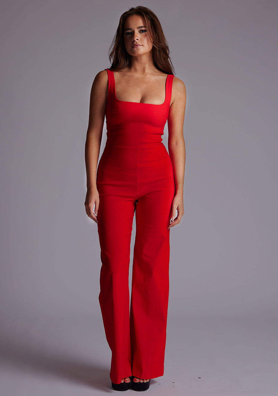 Front image of a model wearing the Vesper Alana Square Neck Wide Leg Jumpsuit in Red, featuring a sleek sleeveless design and sculpted bodice, photographed against a neutral studio backdrop.