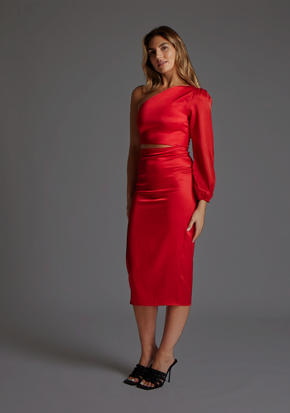 Side front of a model in the Vesper Alice One-Sleeve Midi Dress in Red, highlighting the subtle side waist cut-out, sleek tailored fit, and elegant midi-length silhouette.