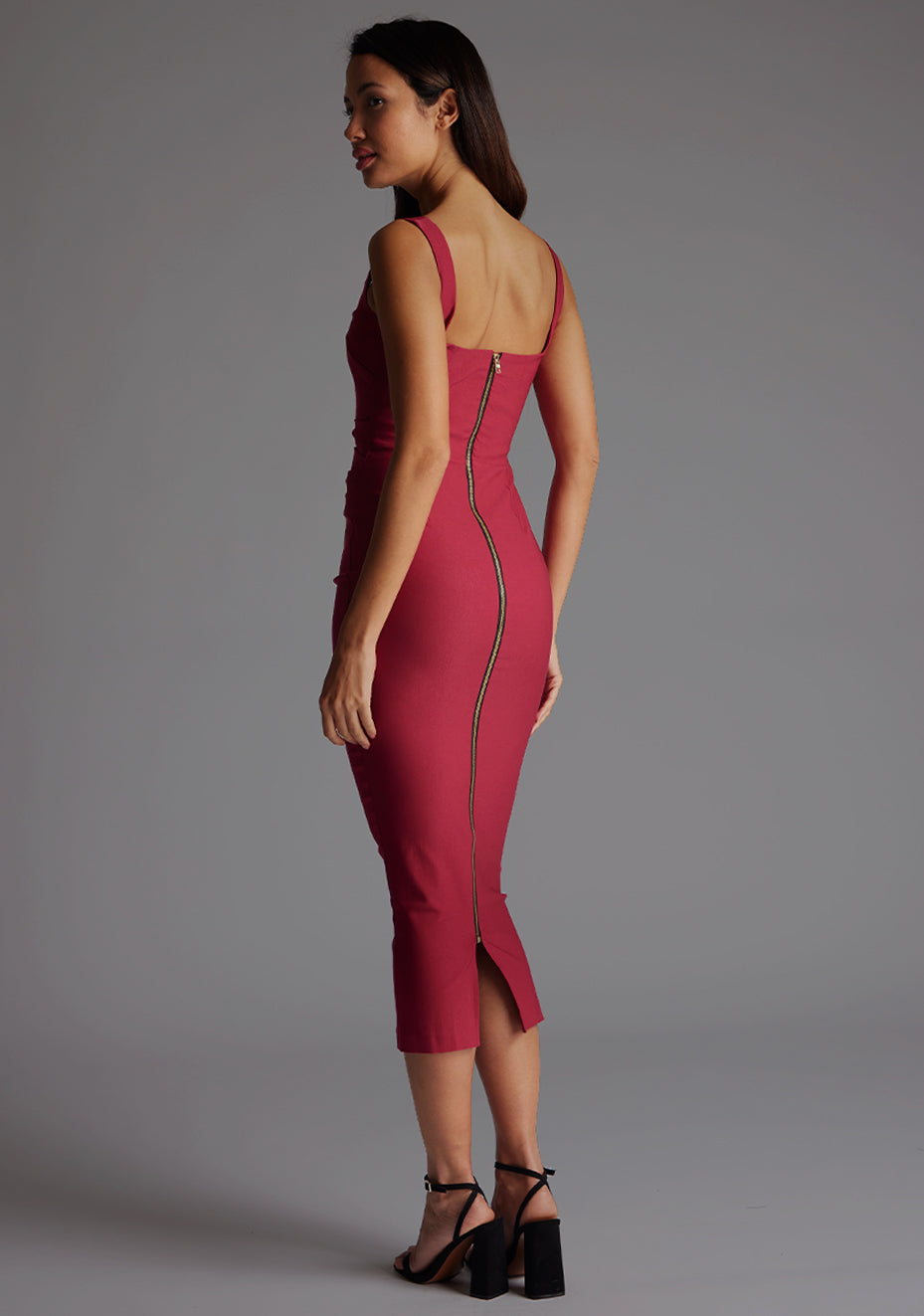 Side back image of a model wearing the Vesper Andy Square Neck Midaxi Dress in Raspberry, revealing the polished gold back zip and subtle back slit.