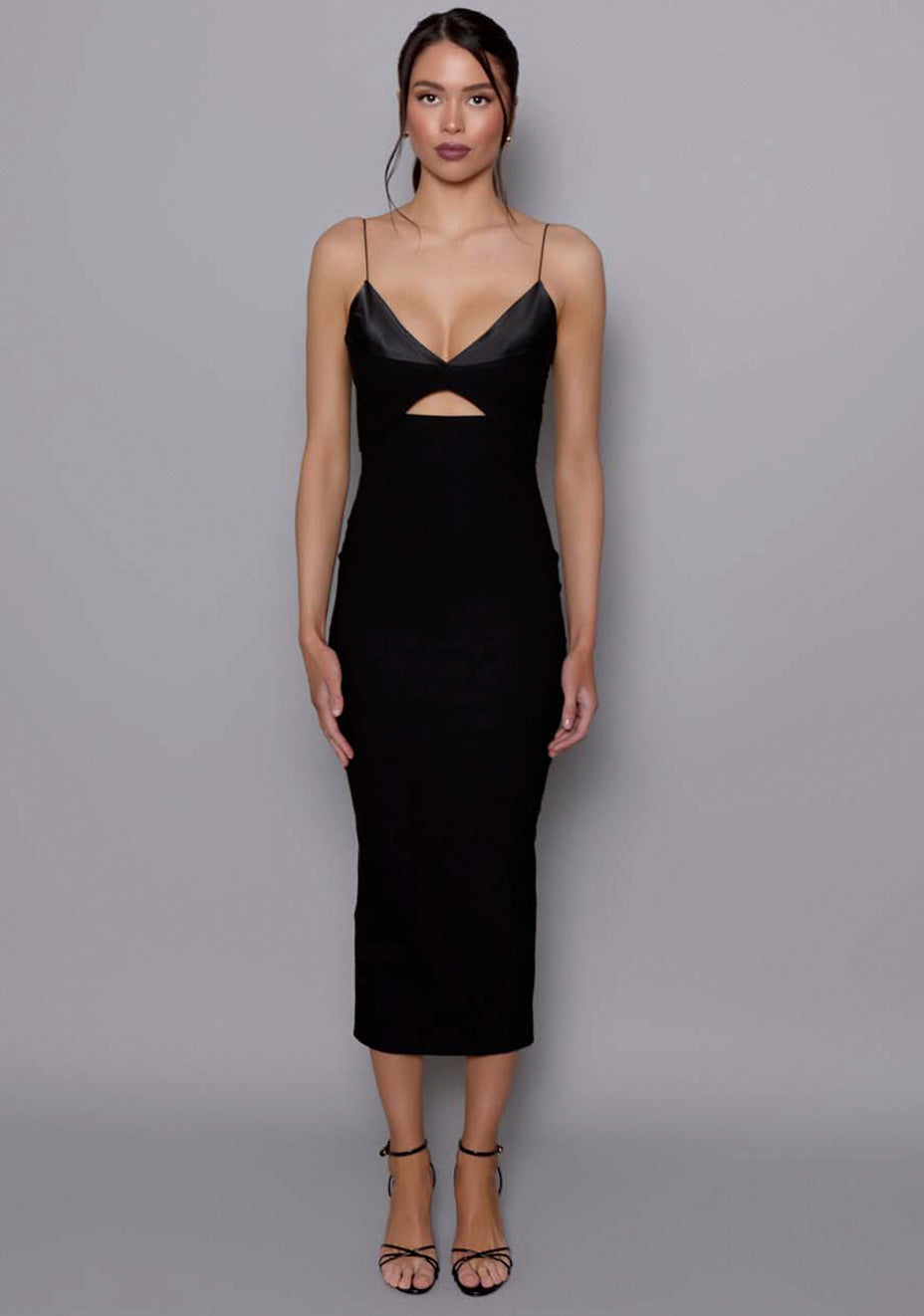 Model wearing the VSPR Angelina black midaxi dress featuring a plunging satin bust, front cut-out, and thin shoulder straps, posed against a neutral grey studio backdrop.