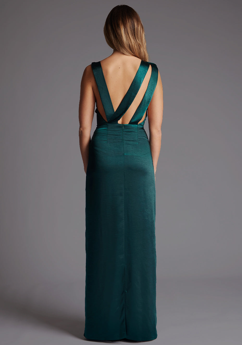 Back view of model wearing a pine green satin maxi dress with dramatic cross-over straps and a deep open back, finished with a long, straight-line maxi skirt.