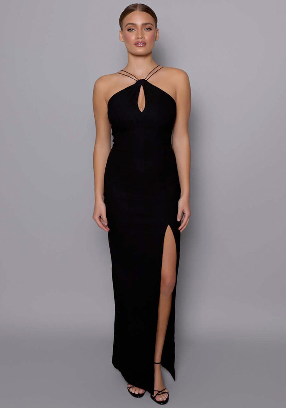 Model wearing the VSPR Auralia black maxi dress featuring a halter neckline, keyhole front cut-out, and slim fit silhouette, styled in a studio setting with a neutral grey backdrop.