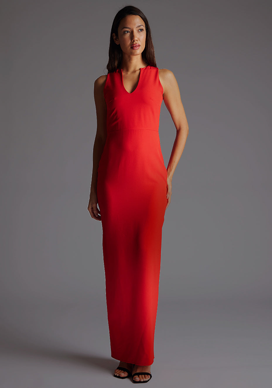 Front image of a model wearing the Vesper Azalea V-Neckline Maxi Dress in Red with a plunging neckline and slim-fit silhouette, standing against a grey studio backdrop.