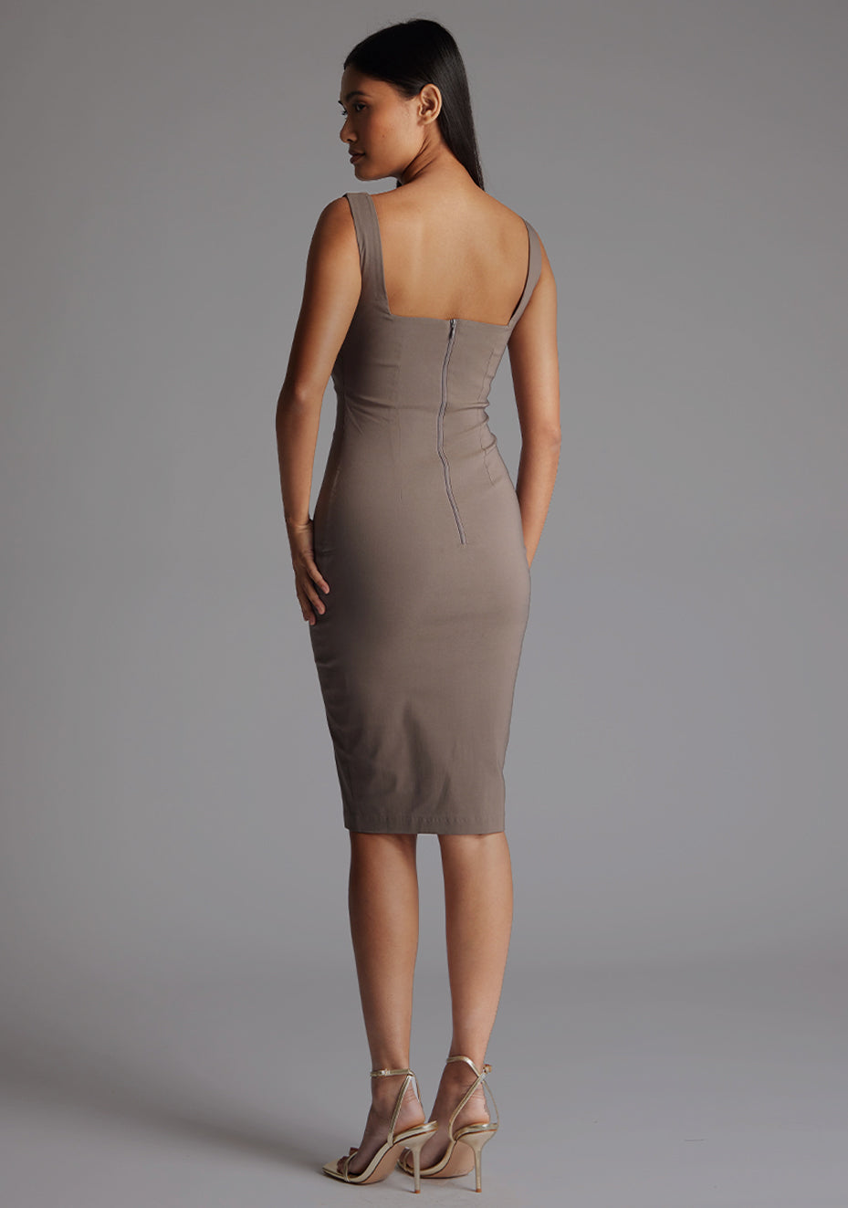 Side back image of a model wearing the Vesper Azzura Bodycon Midi Dress in Taupe, highlighting the elegant bodycon shape and midi-length.