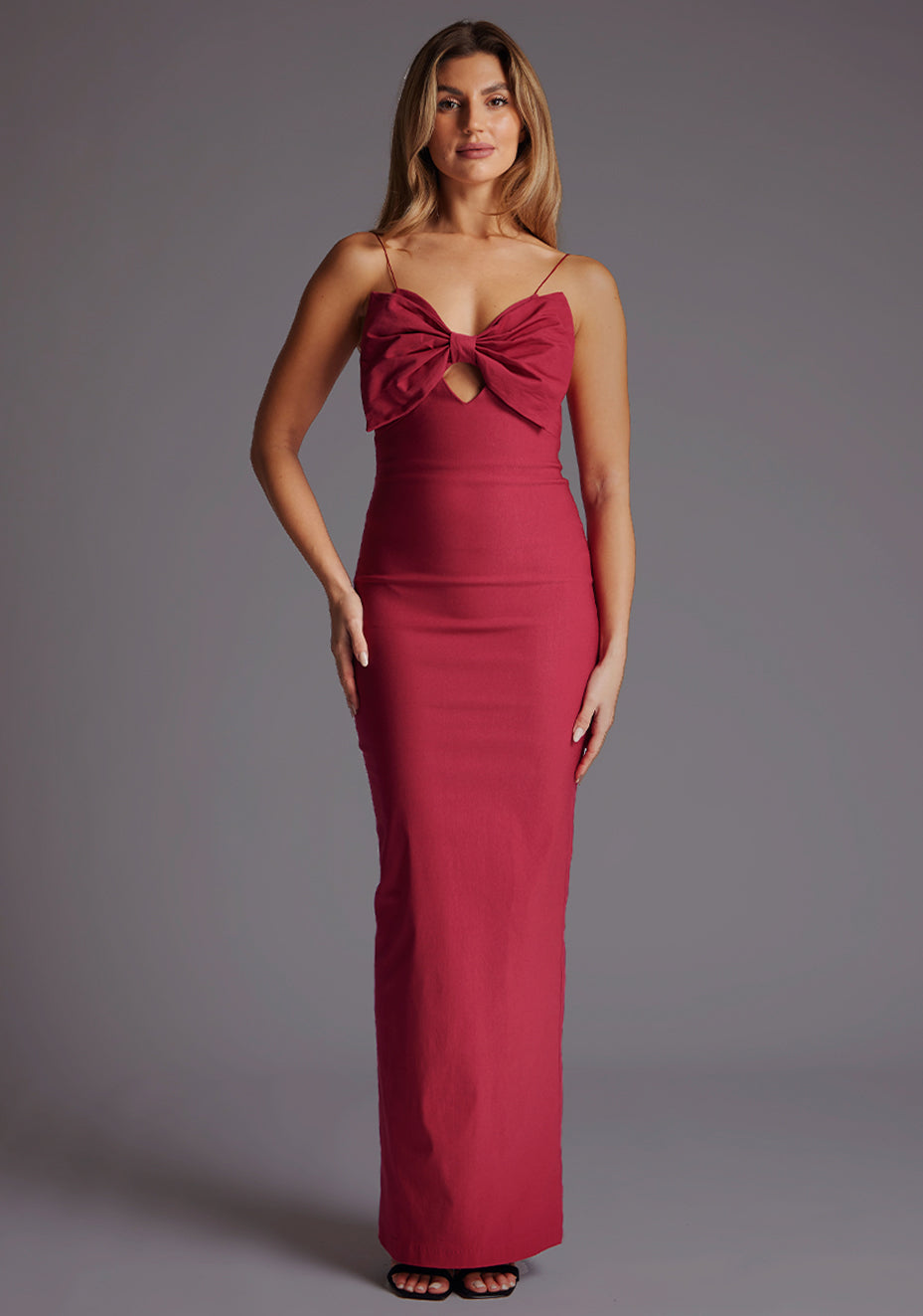 Front image image of a model wearing the Vesper Bellini Cami Strap Bow Maxi Dress in Raspberry, highlighting the delicate cami straps, soft bow detail, and subtle front keyhole, against a grey studio backdrop.