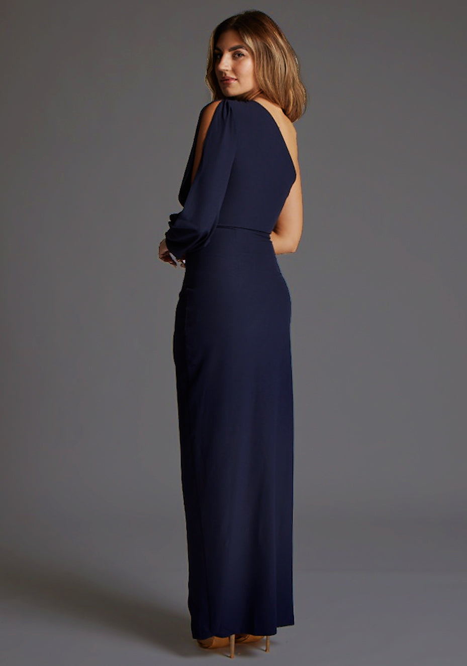 Side back image of a model wearing the Vesper Brooklyn One Shoulder Drape Sleeve Maxi Dress in Navy, revealing the sleek back contour and flowing maxi length.