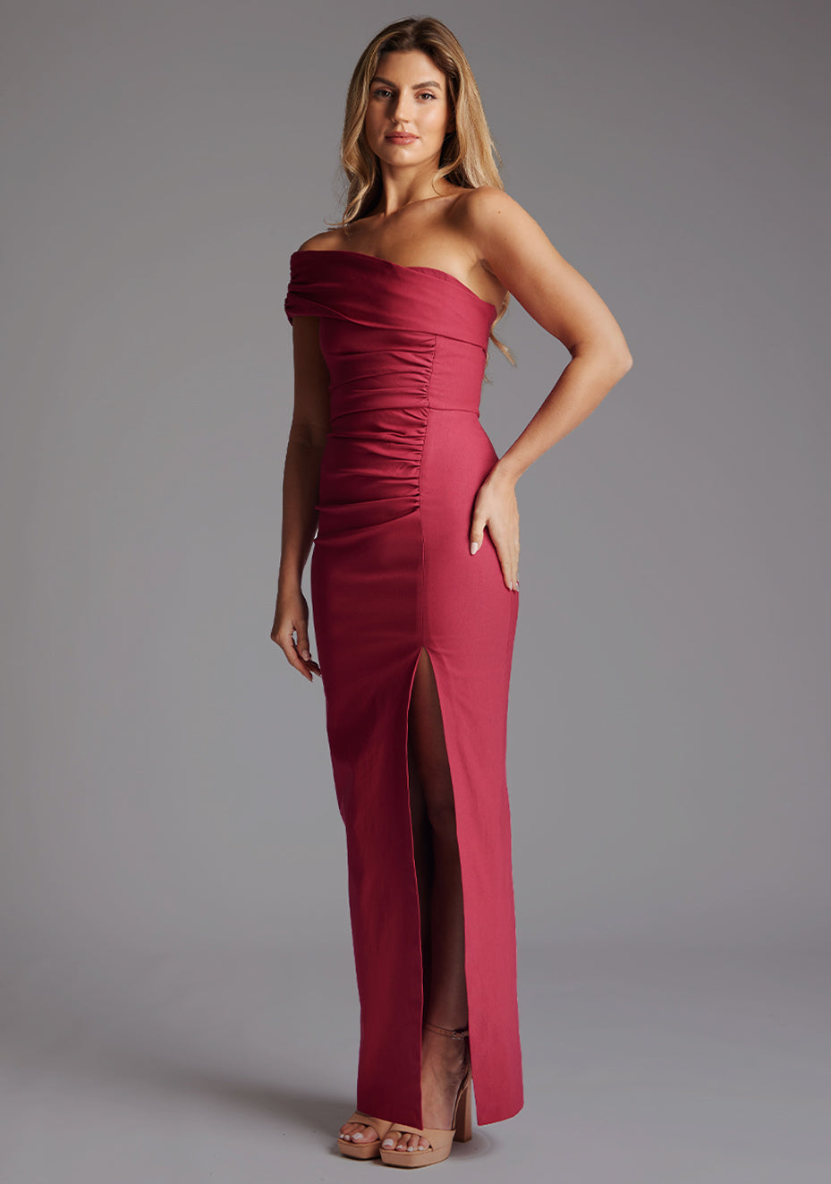 Side front image of a model wearing the Vesper Carmel Off-the-Shoulder Maxi Dress in Raspberry, emphasizing the ruched detailing and fluid asymmetric neckline.