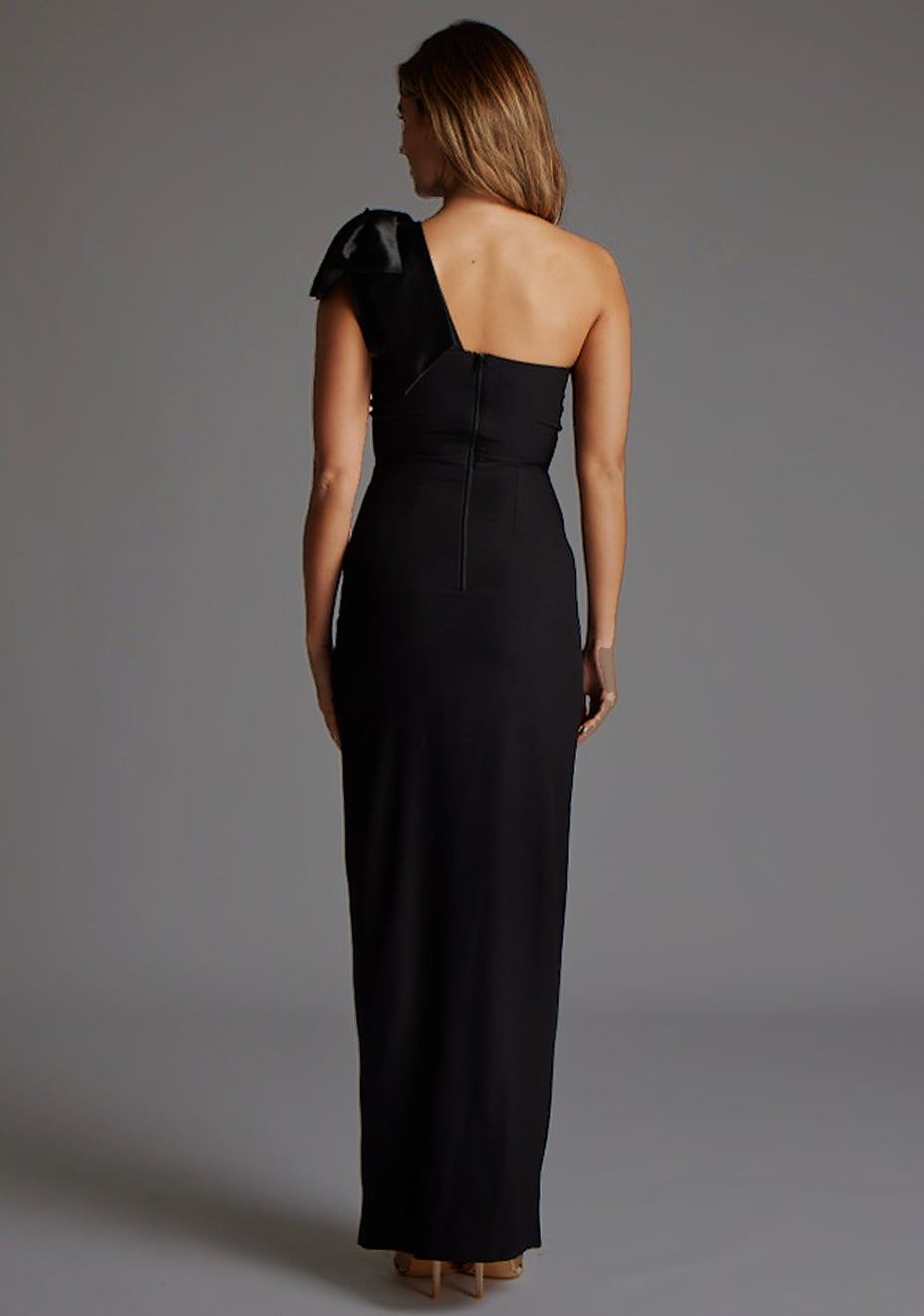 Back image of a model wearing the Vesper Ceylon One Shoulder Bow Maxi Dress in Black, displaying a clean, minimalist back design and full-length maxi skirt.