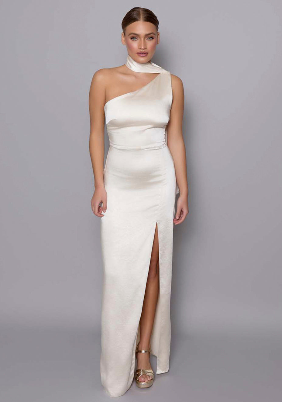 Model wearing the VSPR Cordula cream maxi dress with an asymmetric neckline and satin scarf detail, showcasing the fluid silhouette and luxe satin finish against a neutral studio backdrop.