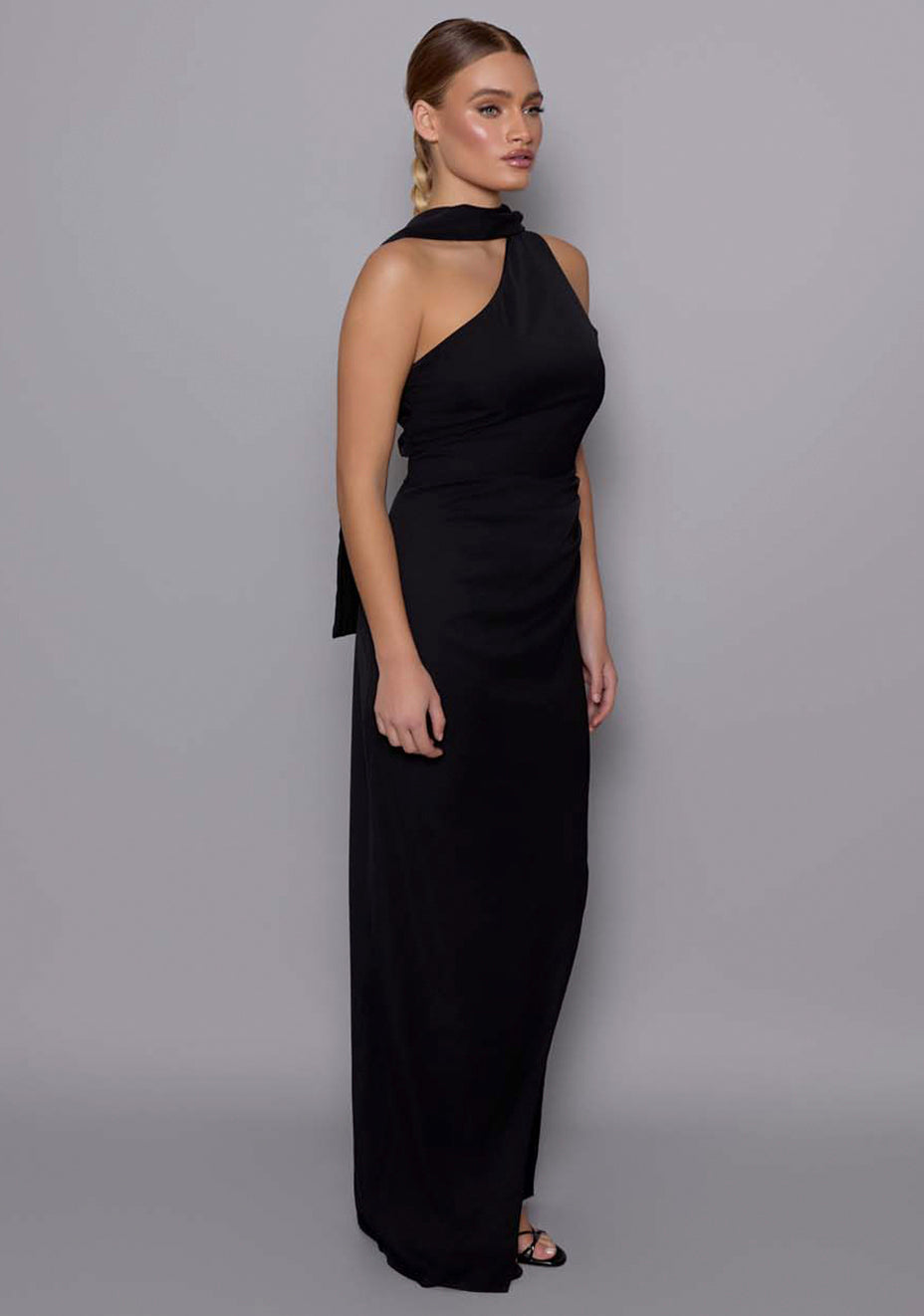 Side-front view of the VSPR Drew black maxi dress showcasing the bodycon fit, asymmetric neckline, and fluid shoulder drape with soft waist contouring.