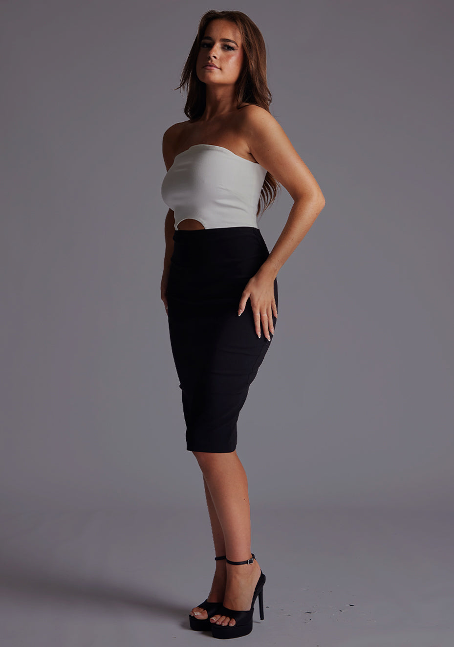 Side front  image of a model wearing a monochrome midi dress with a stunning strapless and the back zipper ensures a comfortable fit. The design featured is the Vesper Drew Strapless Midi Dress in Monochrome.