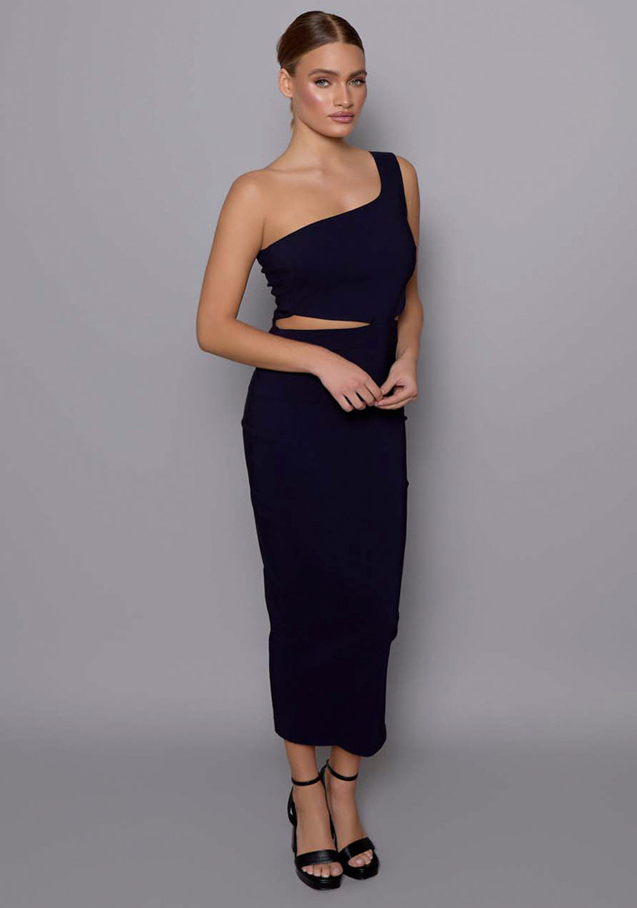 Side-front view of the VSPR Eliza navy dress showing its sculpted silhouette, contoured fit, and statement waist cut-out with one-shoulder styling.