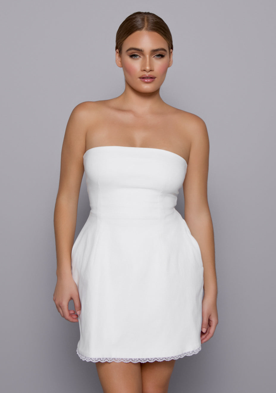 Close-up of the VSPR Emily Dress showing scalloped lace trim along the hem and sculpted bodice, highlighting the soft ivory fabric and romantic detailing.