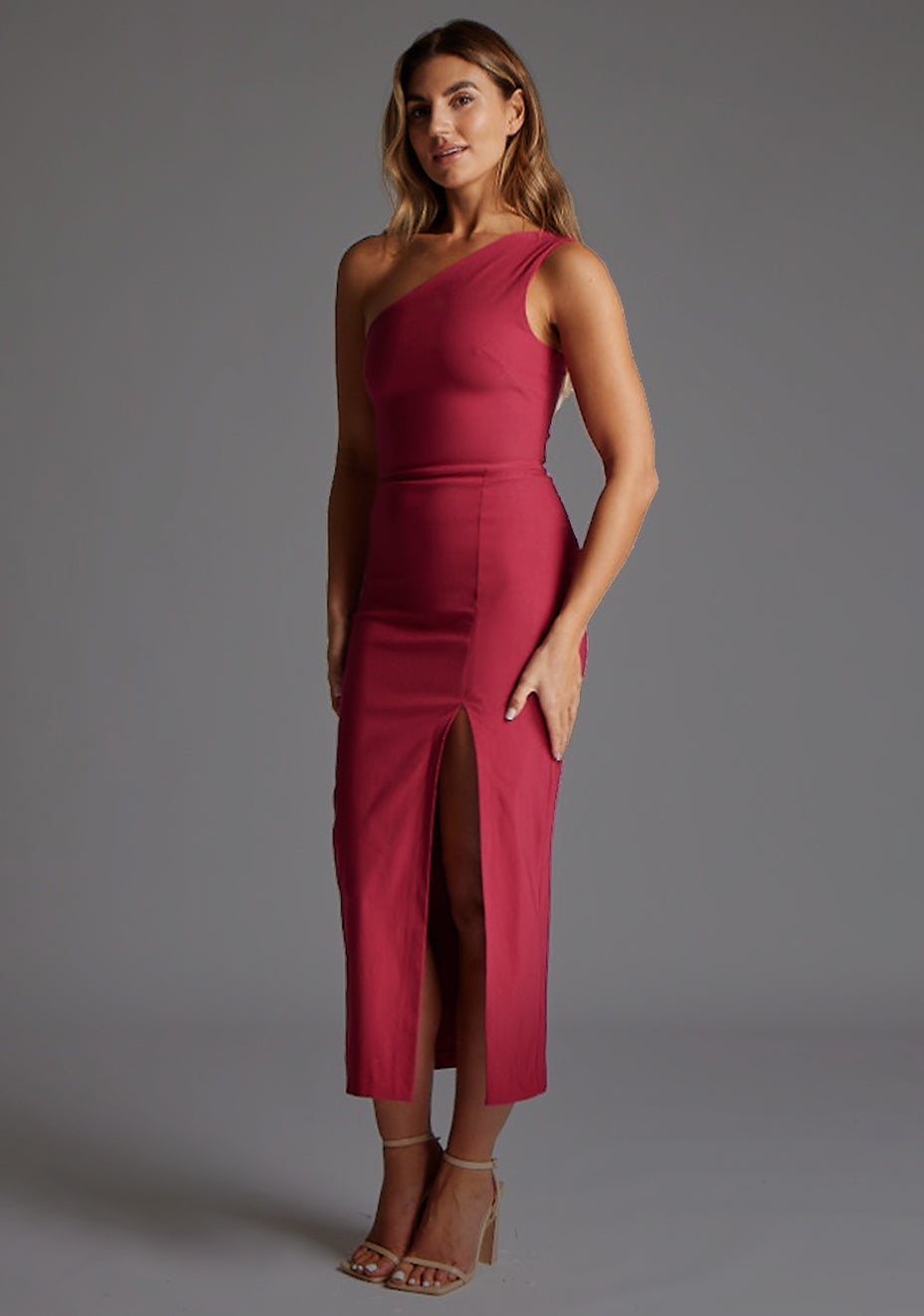 Side front image of blonde model wearing a raspberry one shoulder midaxi dress with a asymmetric neckline, one shoulder and front skirt split. The design featured is the Vesper Gianna One Shoulder Midaxi Dress in Raspberry