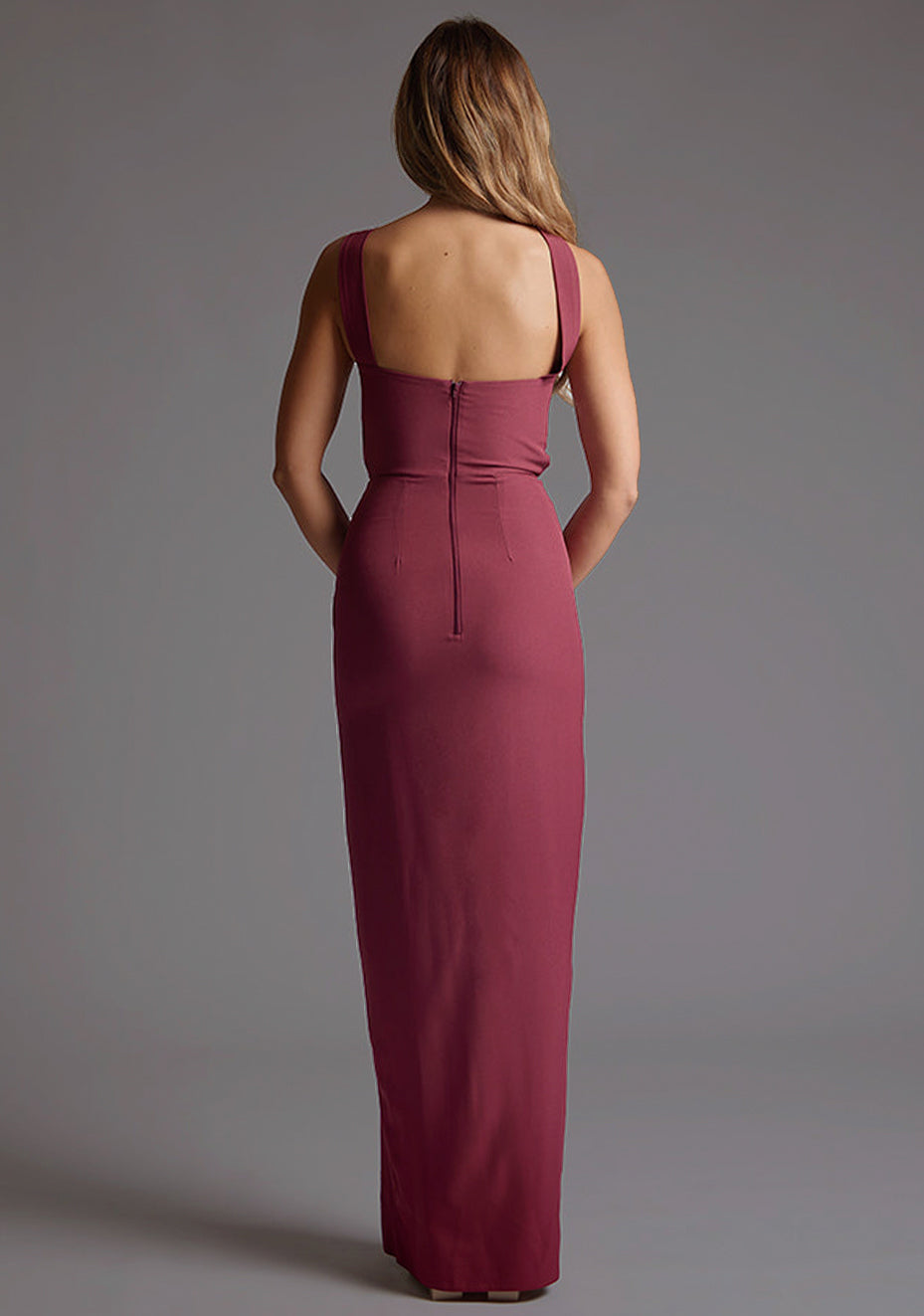 Back image of the model wearing burgundy maxi dress with an alluring one-shoulder asymmetric design, bodycon fit accentuates your curves gracefully and the front skirt split adds a touch of allure. The design featured is the Vesper Gizelle One Shoulder Maxi Dress in Burgundy.