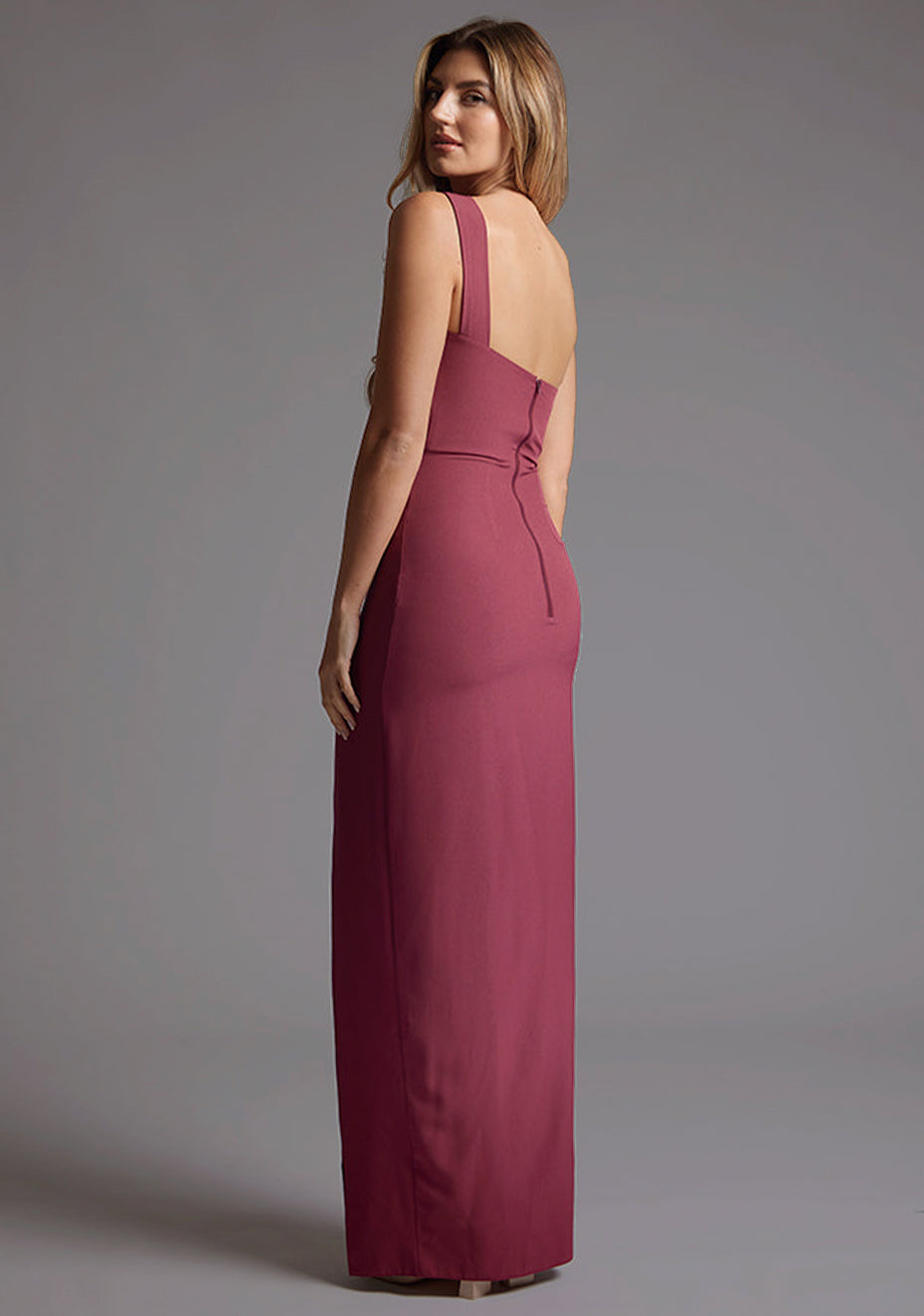 Side back image of the model wearing burgundy maxi dress with an alluring one-shoulder asymmetric design, bodycon fit accentuates your curves gracefully and the front skirt split adds a touch of allure. The design featured is the Vesper Gizelle One Shoulder Maxi Dress in Burgundy.