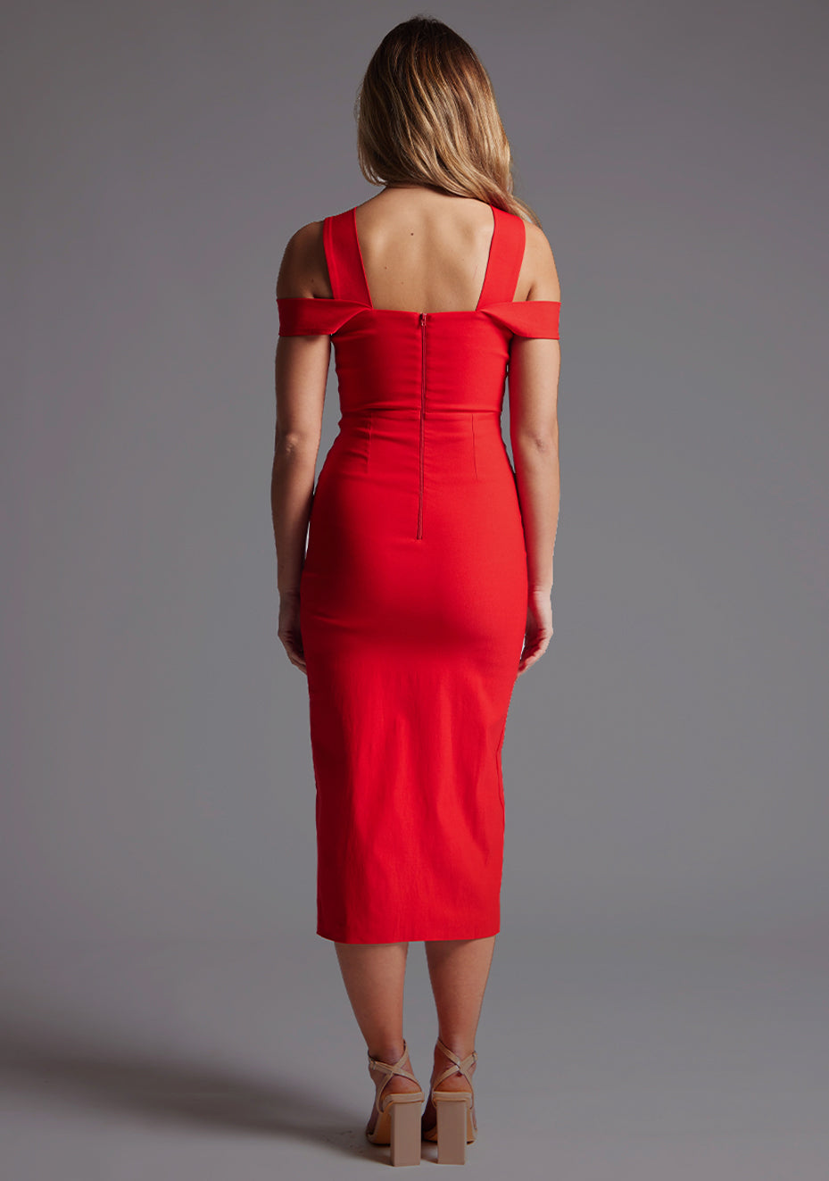 Back image of a model wearing a red midaxi dress with a stylish halter neck design with O-ring detail, adding a touch of uniqueness. The dress also boasts a front split, adding a subtle hint of allure. The design is the Vesper Jadus Halter Neckline Midaxi Dress in Red.