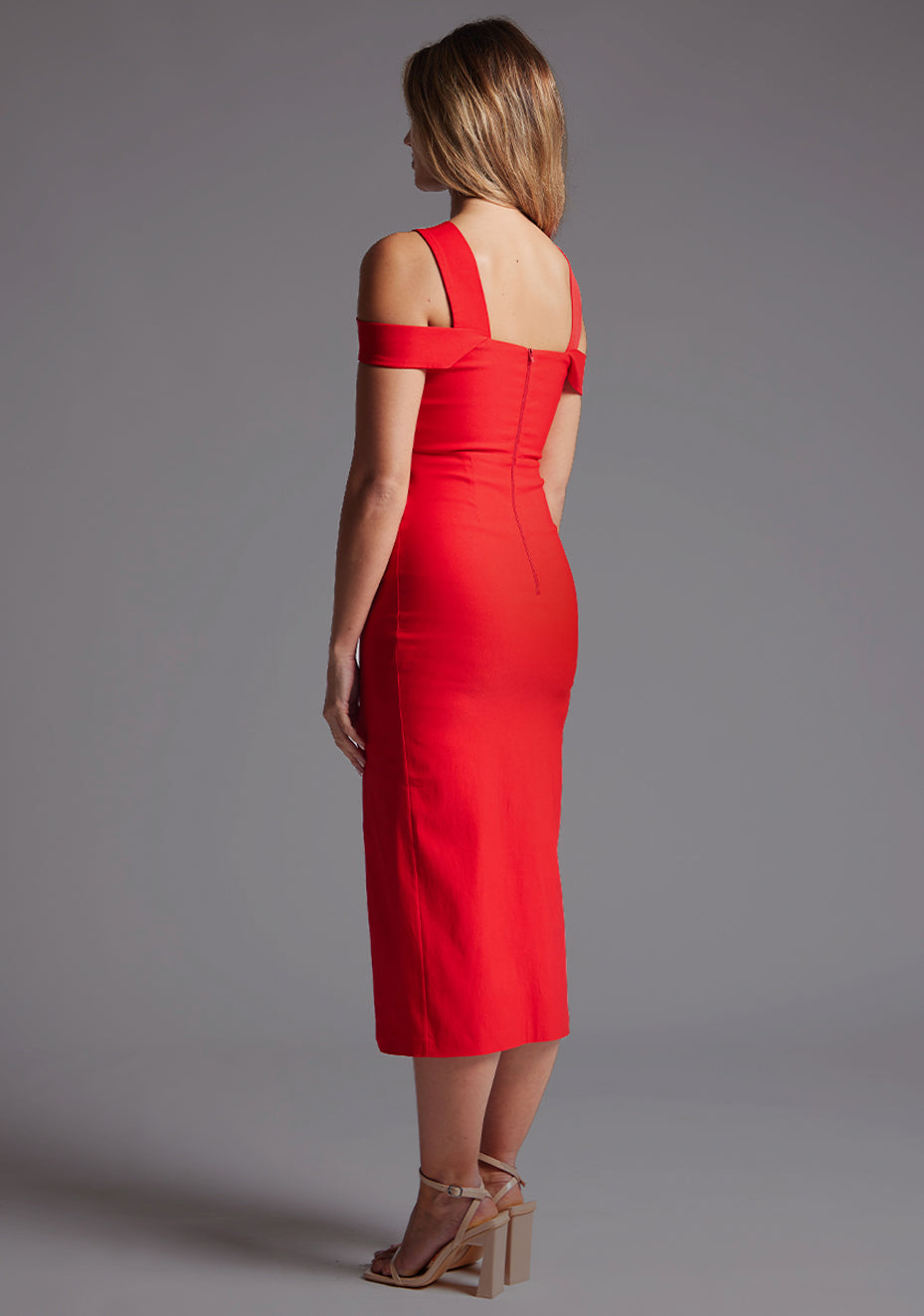 Side back image of a model wearing a red midaxi dress with a stylish halter neck design with O-ring detail, adding a touch of uniqueness. The dress also boasts a front split, adding a subtle hint of allure. The design is the Vesper Jadus Halter Neckline Midaxi Dress in Red.