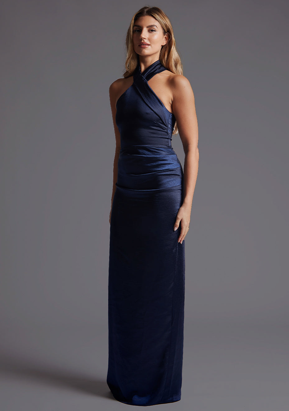 Side front image of model wearing a lake navy maxi dress with a flattering halter neckline, crafted in a rich navy hue, it exudes timeless charm, back slit and invisible centre back zip. The design featured is Vesper Lake Halter Neckline Maxi Dress in Navy.