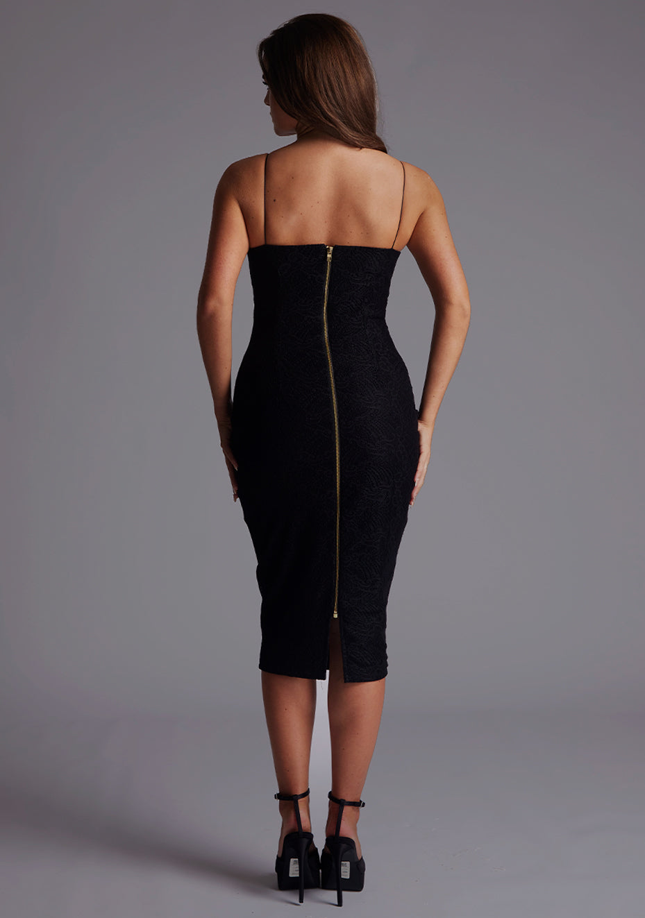 Back image of a model wearing the Vesper Layla Lace Overlay Cami Strap Midi Dress in Black, featuring a statement centre-back gold zip and sleek lace overlay.