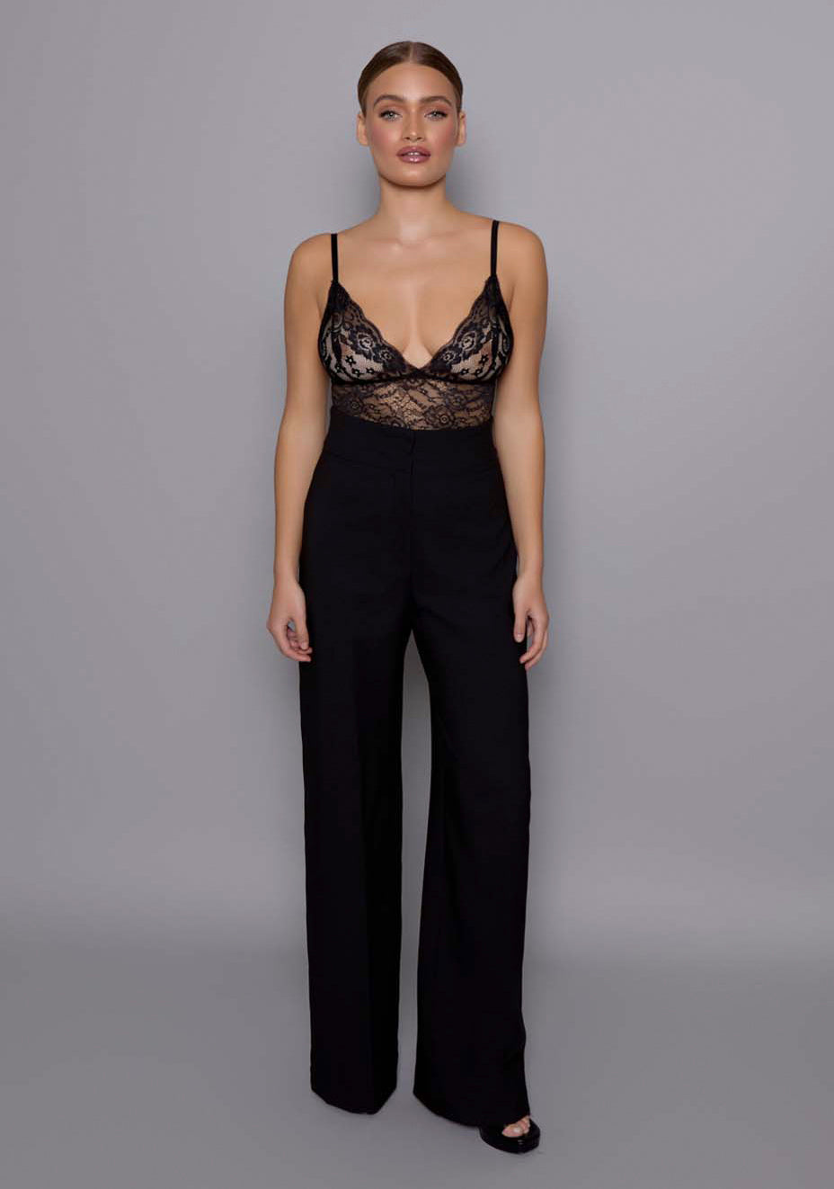 Model wearing the VSPR Lumi high-waist tailored trousers in black with a smooth wide-leg silhouette and structured fit, standing against a neutral studio background.