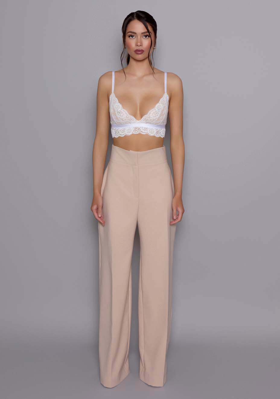 Model wearing the VSPR Lumi High-Waist Tailored Trousers in soft Stone, showing the structured high waist and wide-leg silhouette,  standing against a gray studio backdrop.