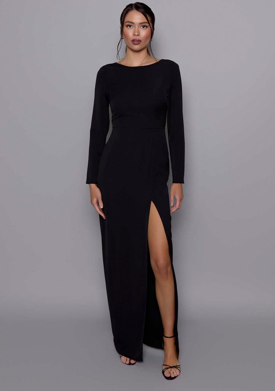 Model wearing the VSPR Mandy Black Maxi Dress with a classic round neckline, long sleeves, and a front skirt split, standing against a neutral studio backdrop.