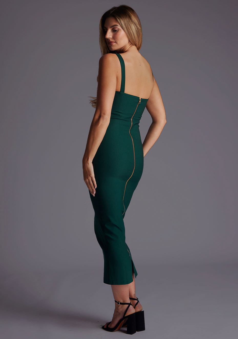Side back image of a blonde model wearing a Forest Green Midaxi Dress with a flattering scoop neckline that accentuates the collarbone and a bodycon silhouette that effortlessly enhances your curves. The design features is the Vesper Marleen Scoop Neck Bodycon Midaxi Dress in Forest Green.