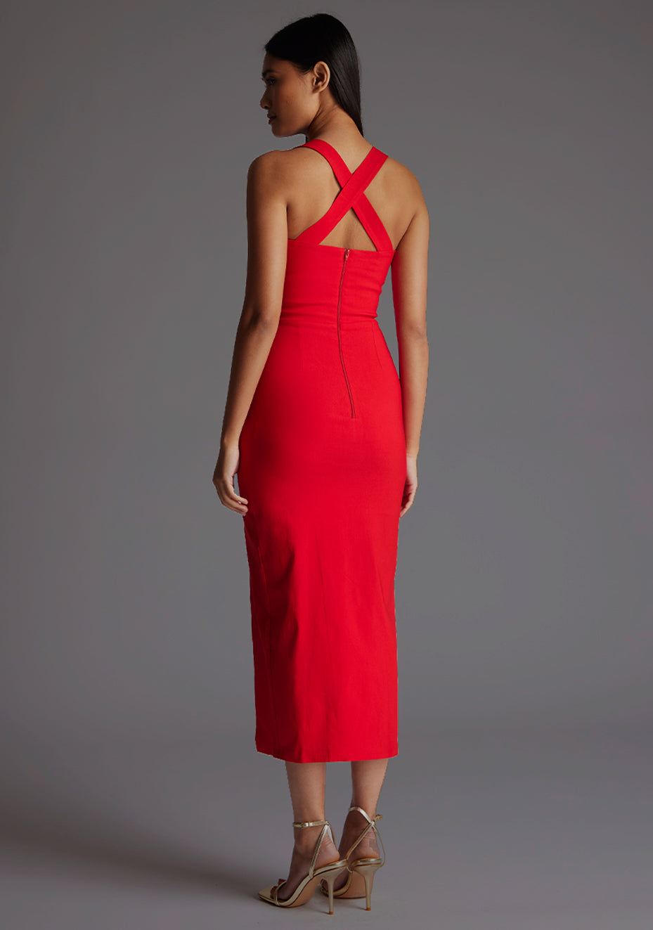 Side back image of a  model wearing a red midaxi dress, featuring plunge sweetheart halter neck straps which cross at the back and a front skirt split. The dress featured is the Vesper Poppy Sweetheart Cross Strap Midaxi Dress in Red.