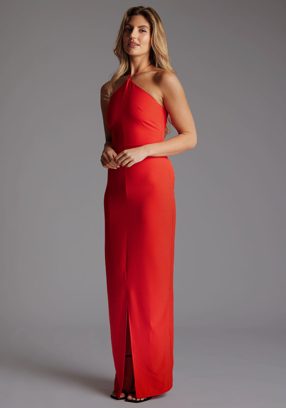Side front image of a model wearing the Vesper Sadie Halter Neck Maxi Dress in Red, highlighting the flowing maxi skirt, centre-front split, and sculpted fit.