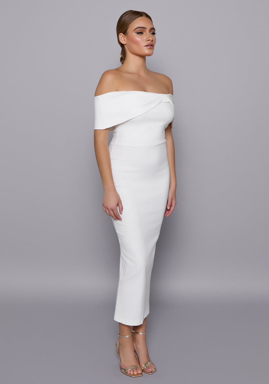Side-front view of the VSPR Sarah Ivory Midaxi Dress showing the curve-enhancing bodycon silhouette, structured neckline, and delicate off-shoulder band.