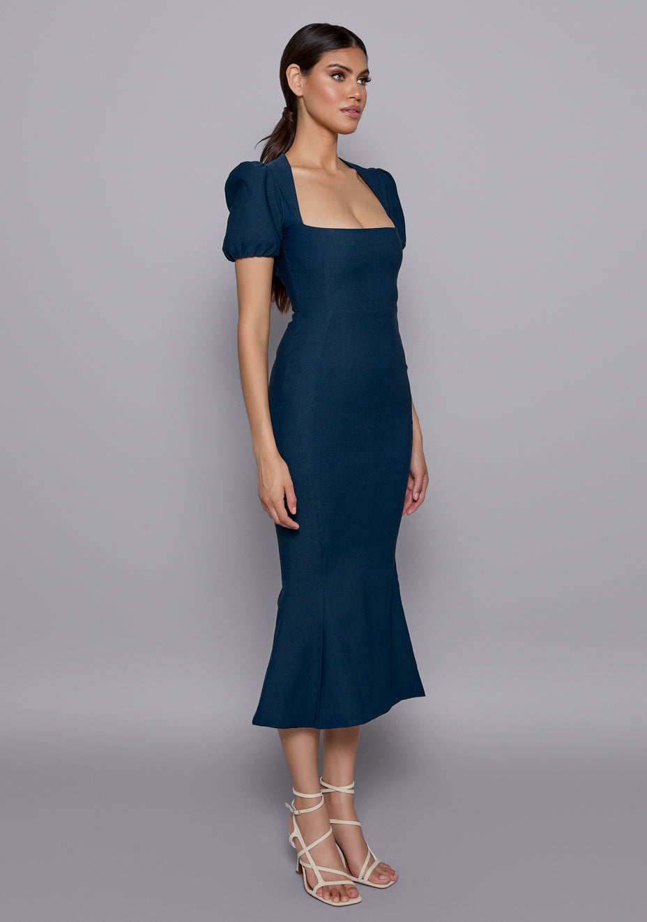 Side-front view of the VSPR Valencia Fishtail Navy Dress showcasing the fitted bodice, romantic puffed sleeves, and gentle flare of the fishtail hem.