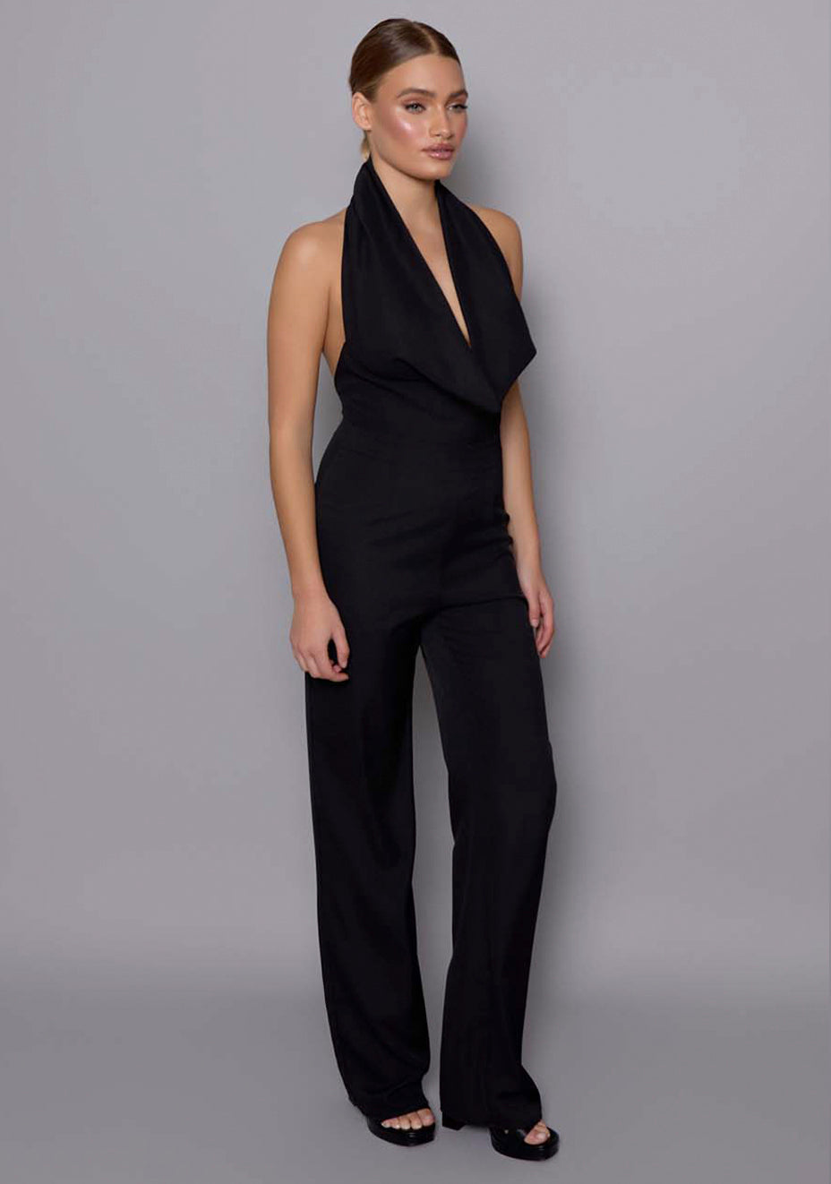 Side front view of the VSPR Zinna Black Jumpsuit revealing the flattering silhouette, fitted sleeves, and wide-leg design for a refined evening look.