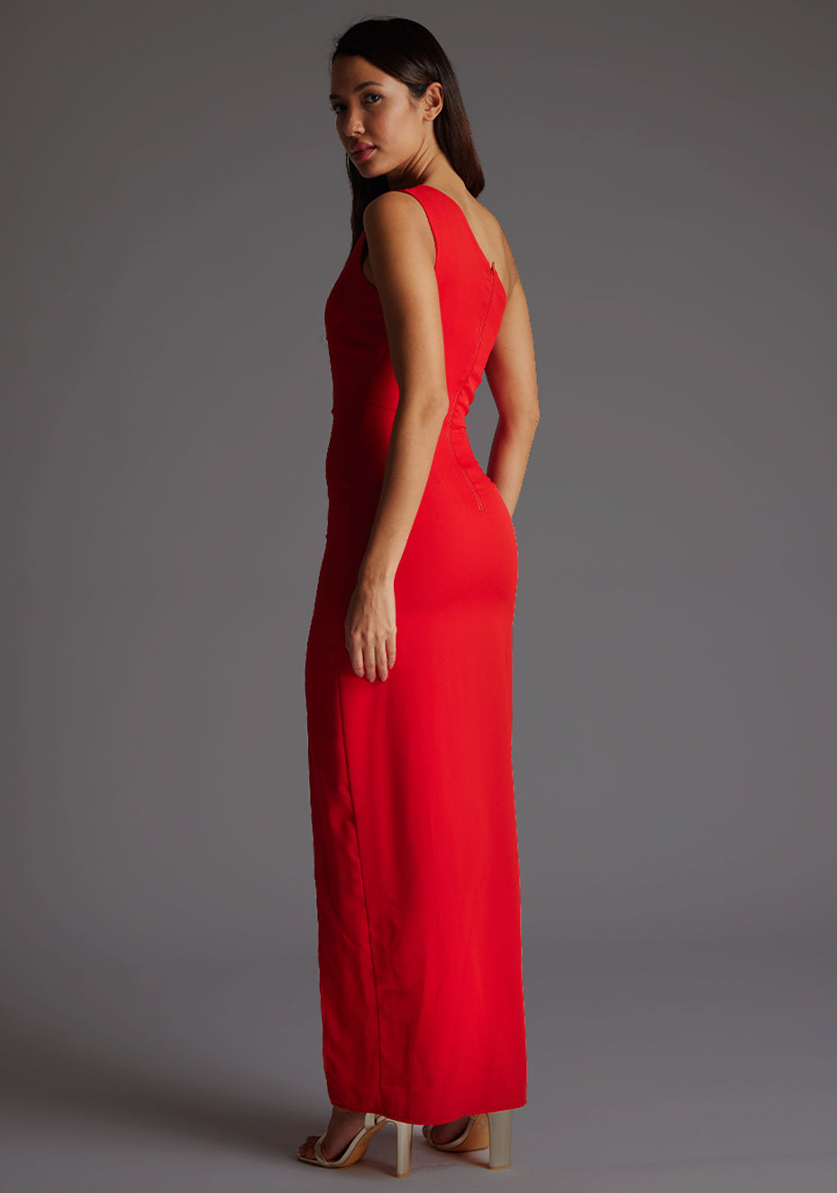 Back quarter image of model wearing red asymmetric maxi dress with a asymmetric neckline with one shoulder detail, front bodice cut-out and front skirt split. The design featured is Vesper Verity Red Asymmetric Maxi Dress