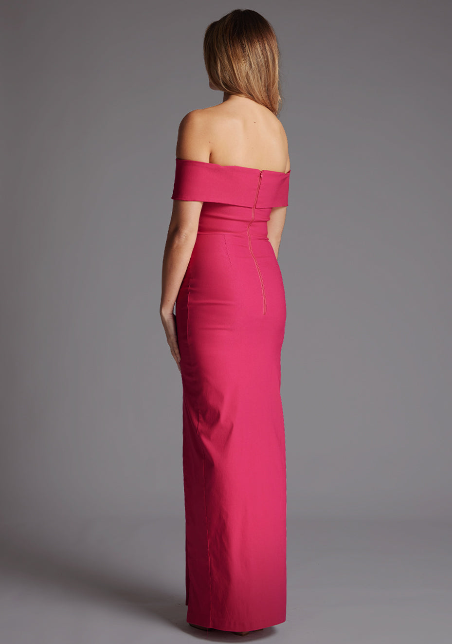 Back quarter mage of a model wearing a cerise maxi dress with a sweetheart neckline with curved band detail at bust, beck line at top of arms and finished with a front skirt split. The design featured is the Vesper Ivory Cerise Maxi Dress
