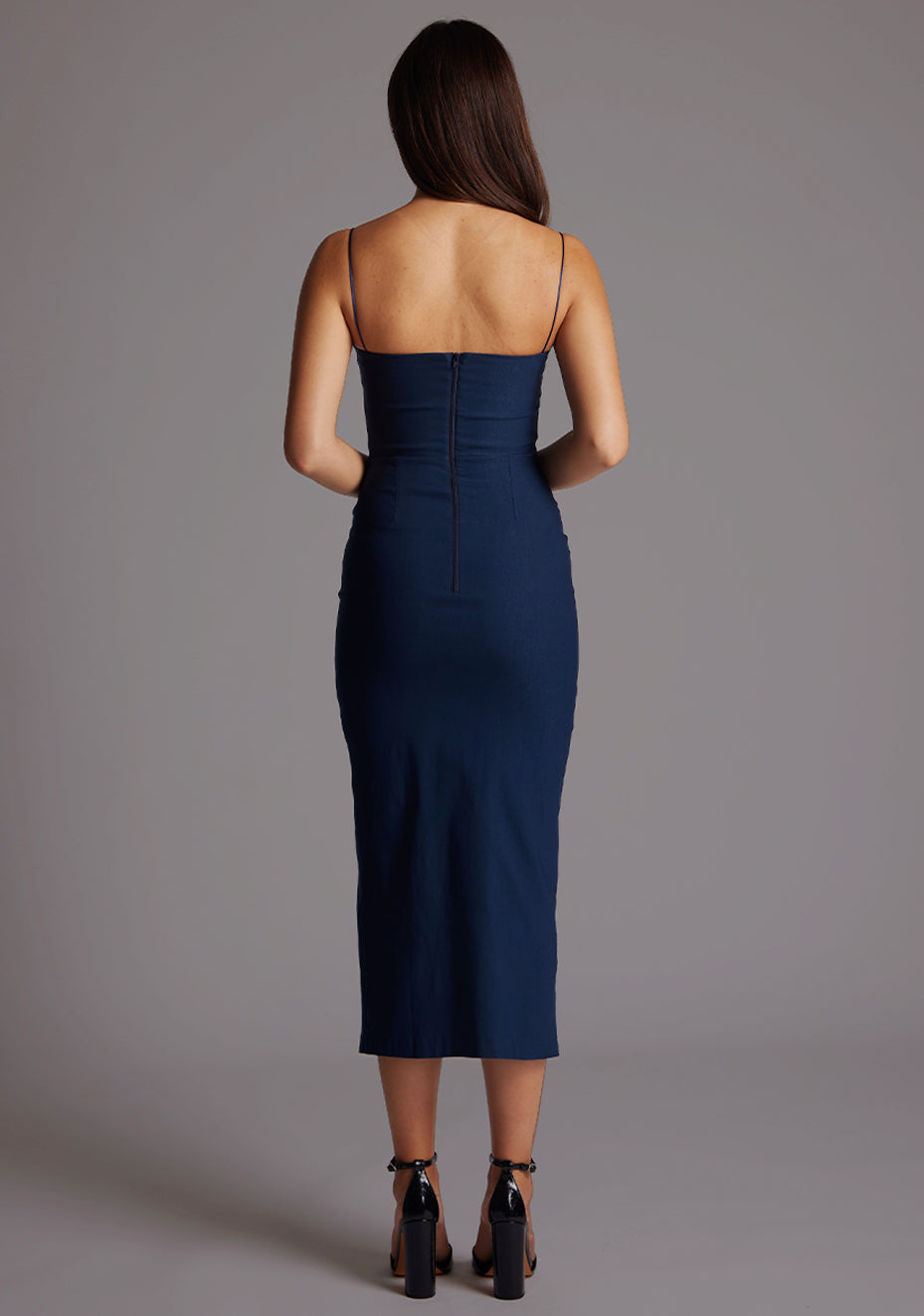 Back image of a model wearing a navy midaxi dress with a timeless design boasts a subtle sweetheart neckline and sophisticated front cut-outs. The graceful front skirt split adds allure. The design featured is the Vesper Kendall Navy Midaxi Dress