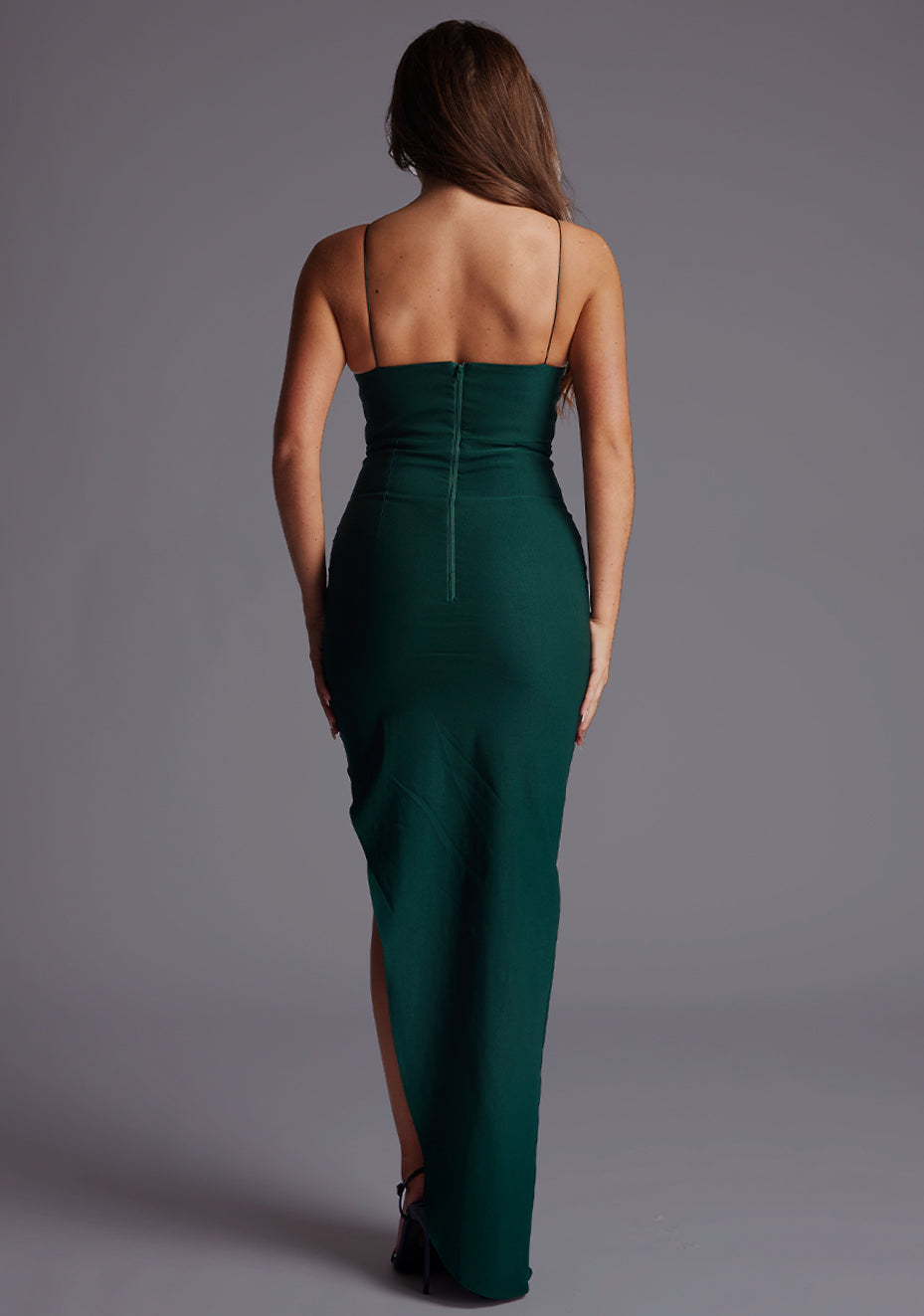 Back image of a blonde model wearing a forest green maxi dress with a delicate thin straps, captivating v-neckline and front cut-out adds a touch of intrigue. The design featured is the Vesper Medina Forest Green Maxi Dress