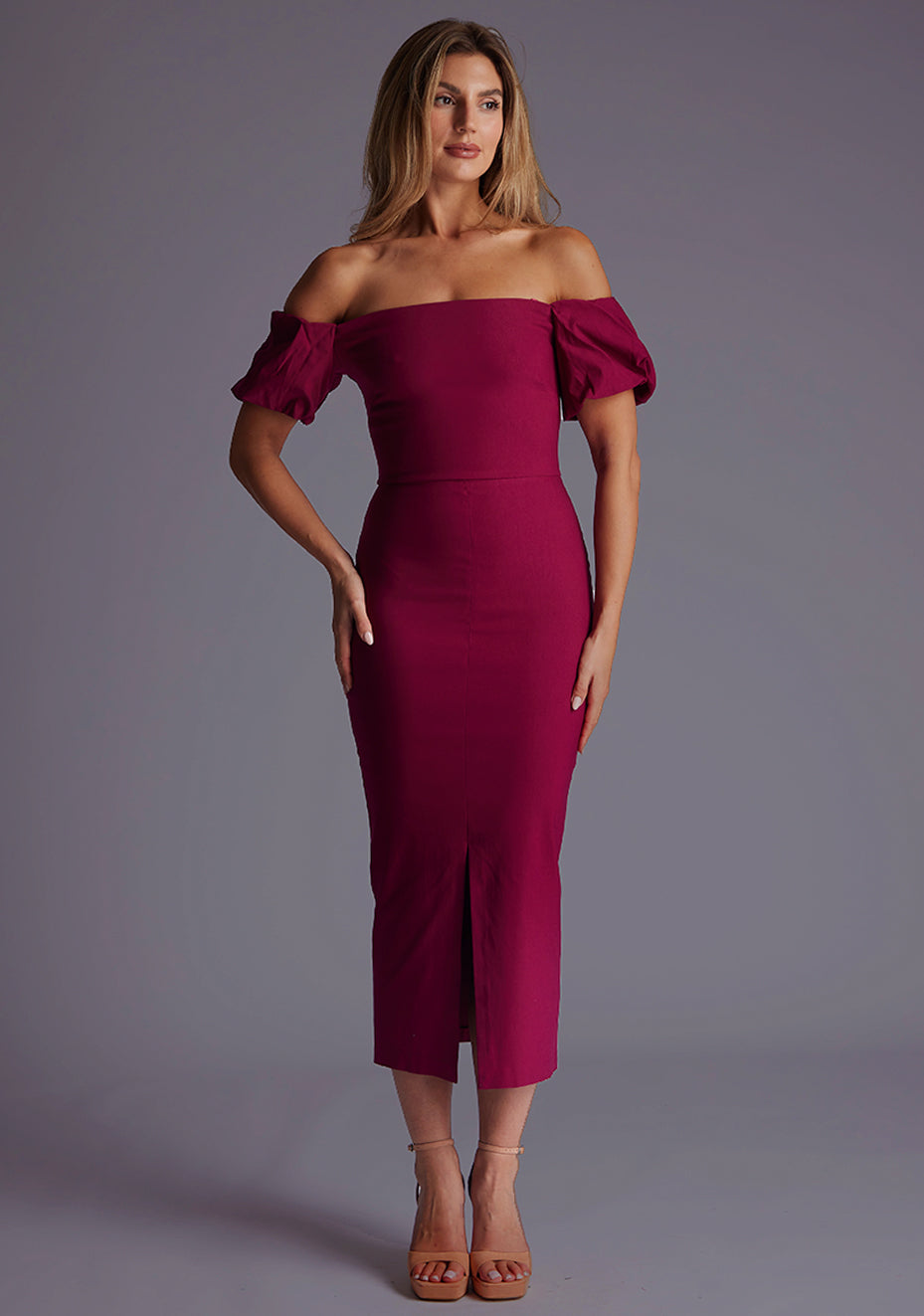 Front image of a blonde model wearing a berry midaxi dress with a bardot neckline gracefully frames the shoulders, while the back zip ensures a seamless silhouette. The design featured is the Vesper Quinton Berry Midaxi Dress.