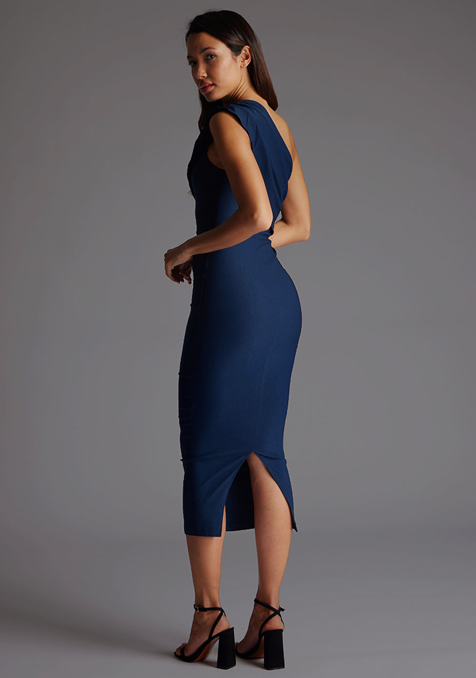Back quarter image of the model wearing a navy midaxi dress with a one-shoulder silhouette exudes confidence design, a asymmetric cut and a bodycon fit. The design featured is the Vesper Rena Navy One Shoulder Midaxi Dress.